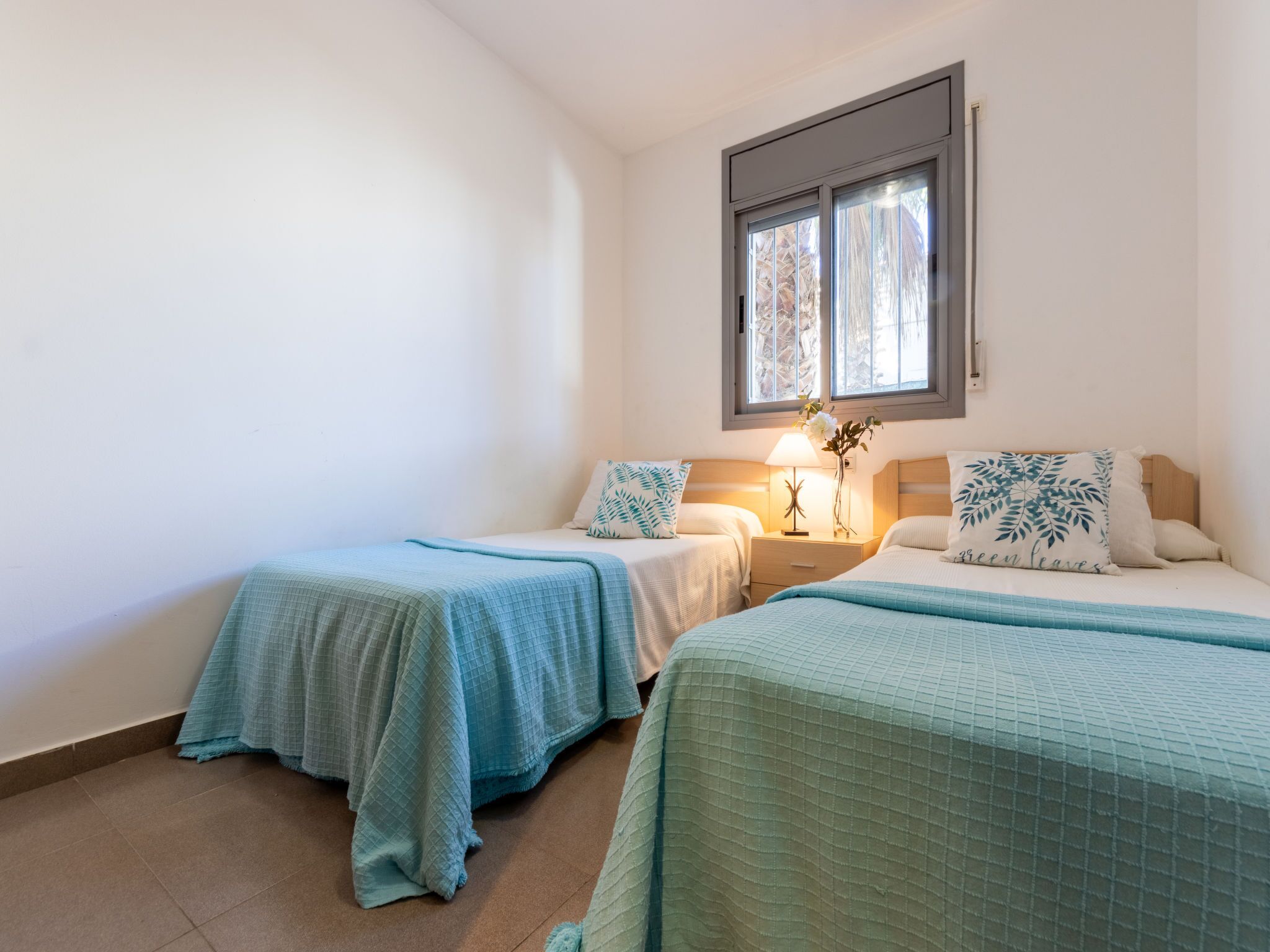 A room with two beds, each with a blue bedspread and matching pillows. There is a nightstand with a lamp between the beds.