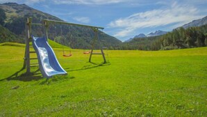 A playground with a slide and swings in a grassy field with mountains in the background. - Schmittnhof by Interhome (Umhausen)