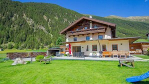 A two-story chalet with a balcony, surrounded by a grassy yard and a blue slide. - Schmittnhof by Interhome (Umhausen)