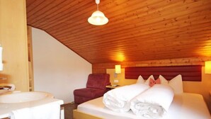 A bedroom with a wooden ceiling, a bed with white linens, a red chair, a bedside table, and a wall-mounted lamp. - Schmittnhof by Interhome (Umhausen)
