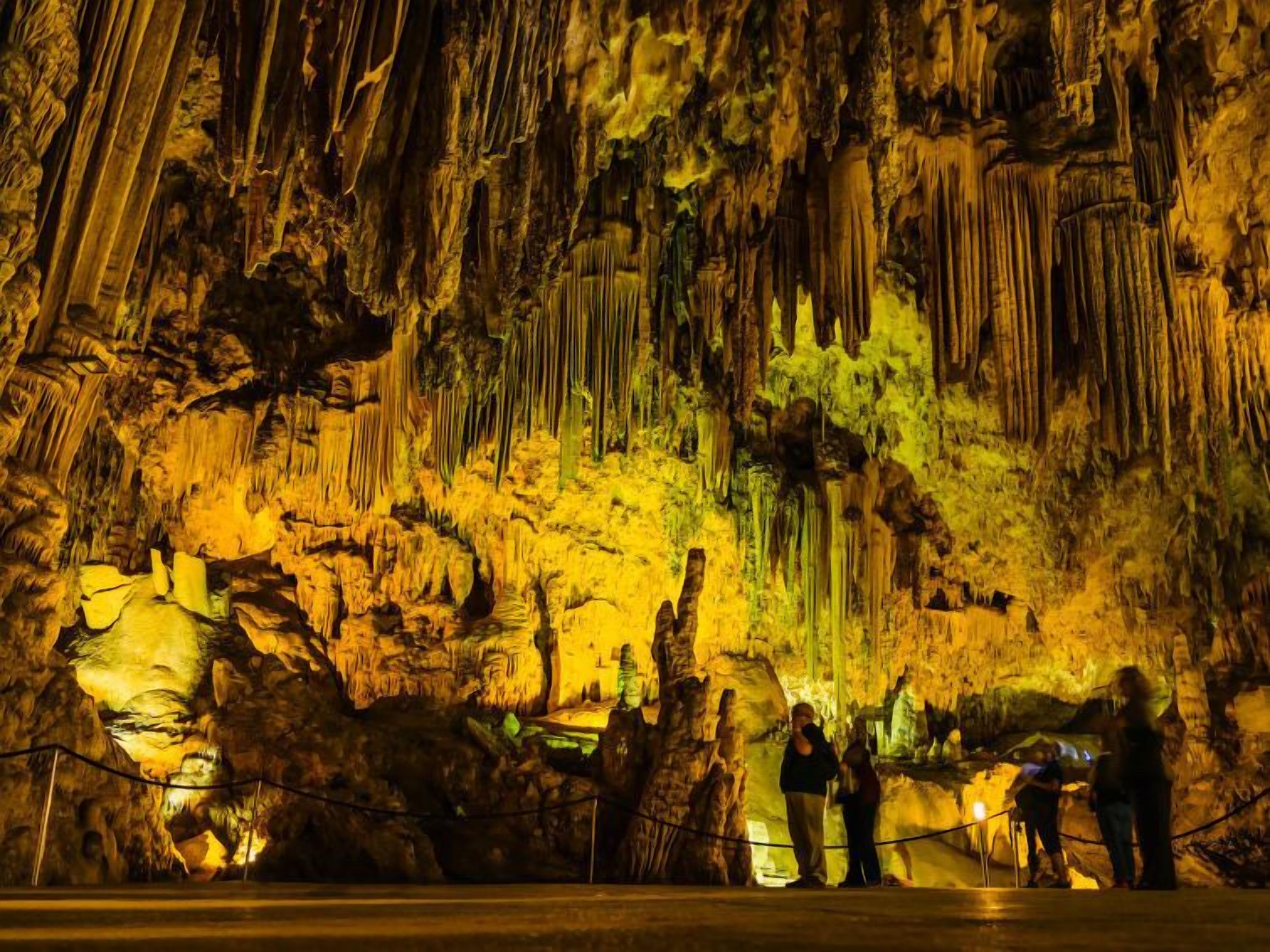 Una grotta con stalattiti e stalagmiti, illuminata da luci artificiali.