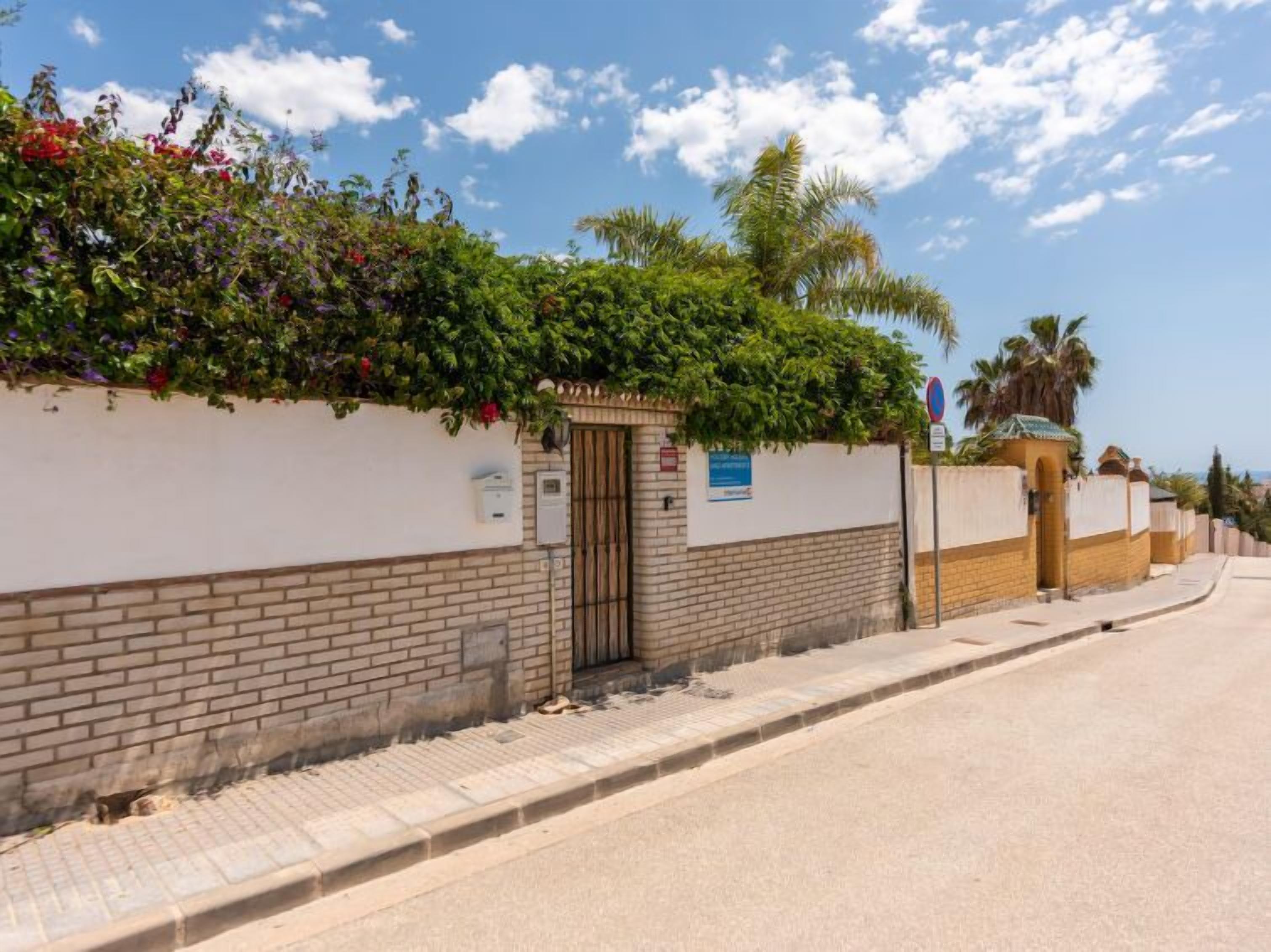 A street with a white wall, a brick section, and a metal gate.