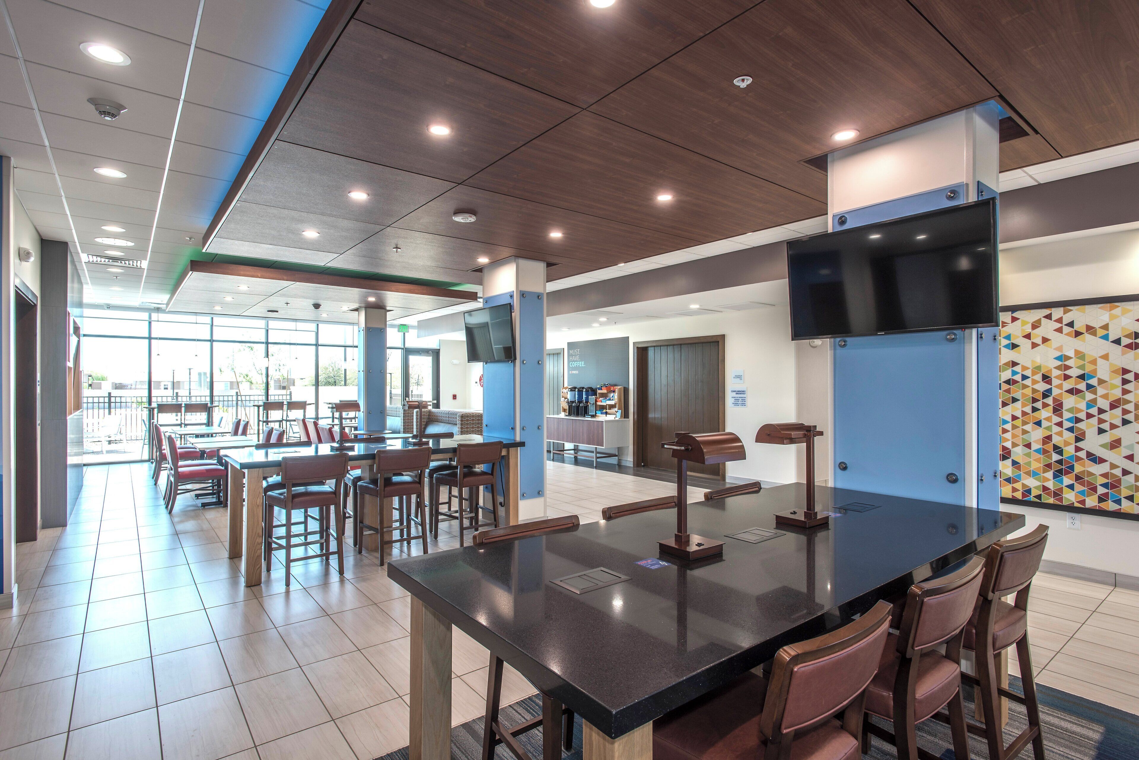 A modern cafeteria with a long communal table, individual seating, and a large screen.