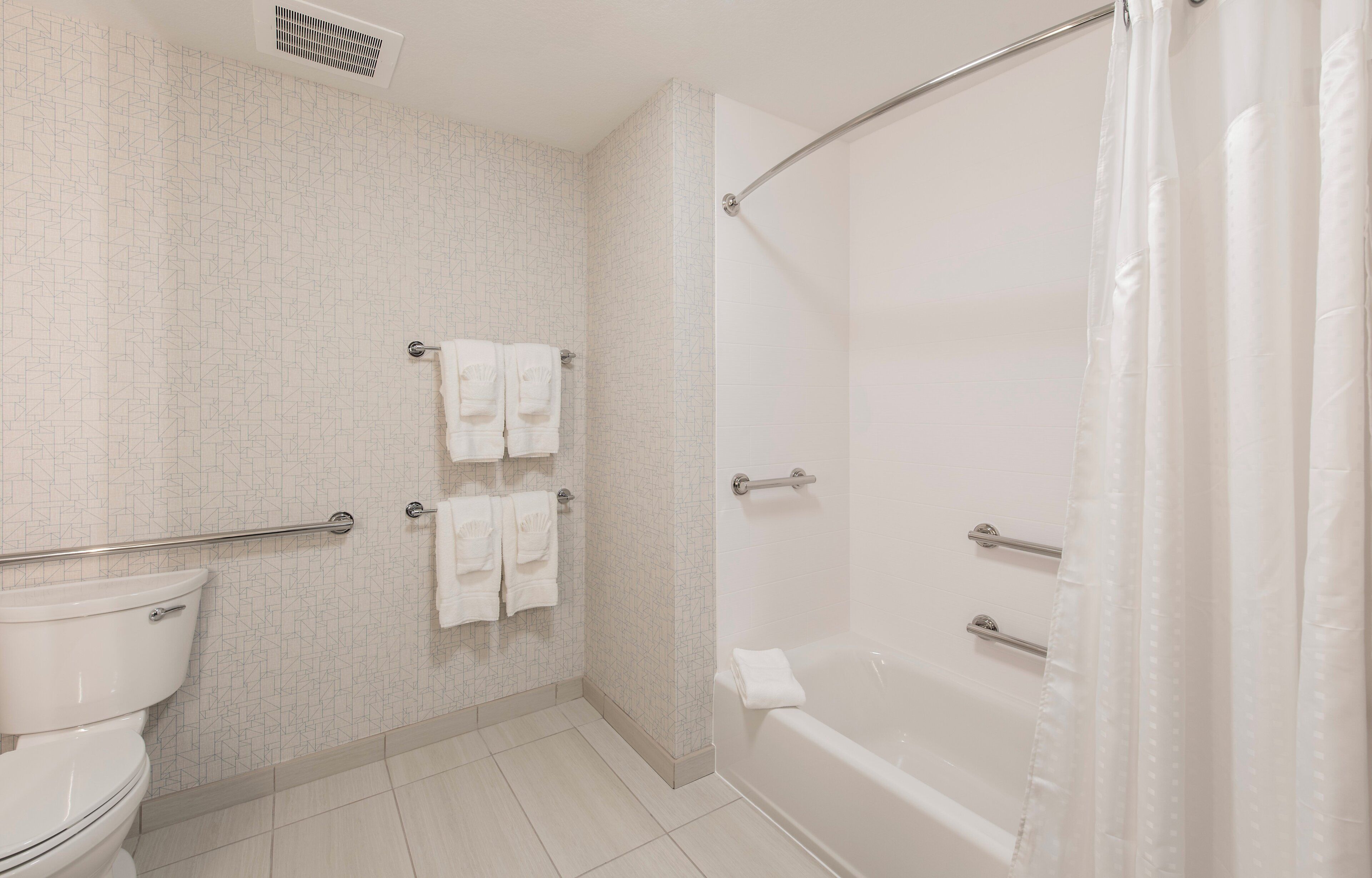 A bathroom with a toilet, a shower with a glass door, and two towel racks with towels.
