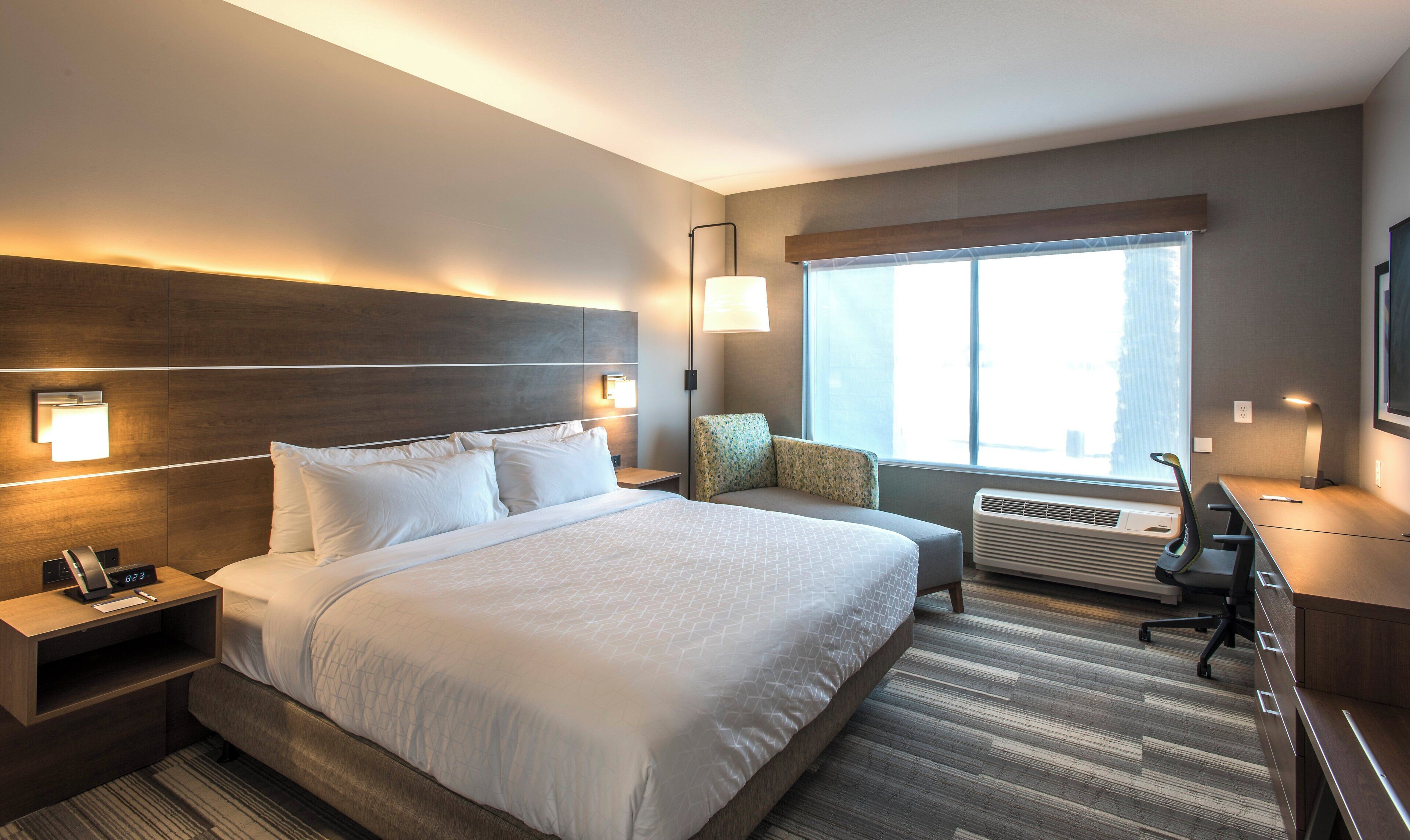 A hotel room with a large bed, bedside tables, a desk, and a window with a view.