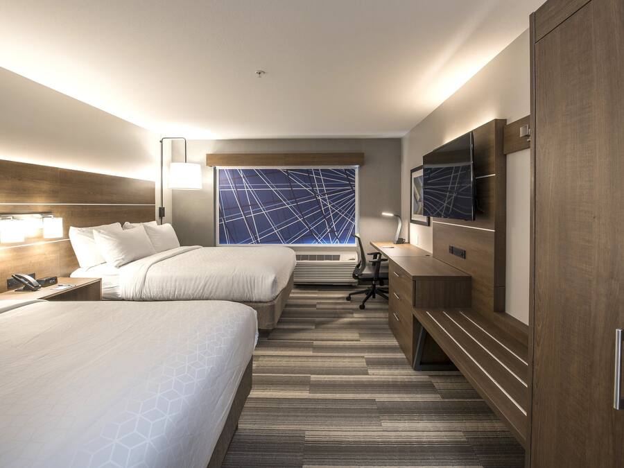 A hotel room with two beds, a desk, a TV, and a large window with a geometric view.