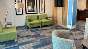 A hotel lobby with a green sofa, a blue armchair, a floor lamp, and framed artwork on the wall. - Holiday Inn Express & Suites Phoenix North - Happy Valley by IHG (Phoenix)