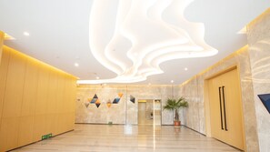 A modern lobby with a marble floor, a large wall-mounted light fixture, and geometric wall art.