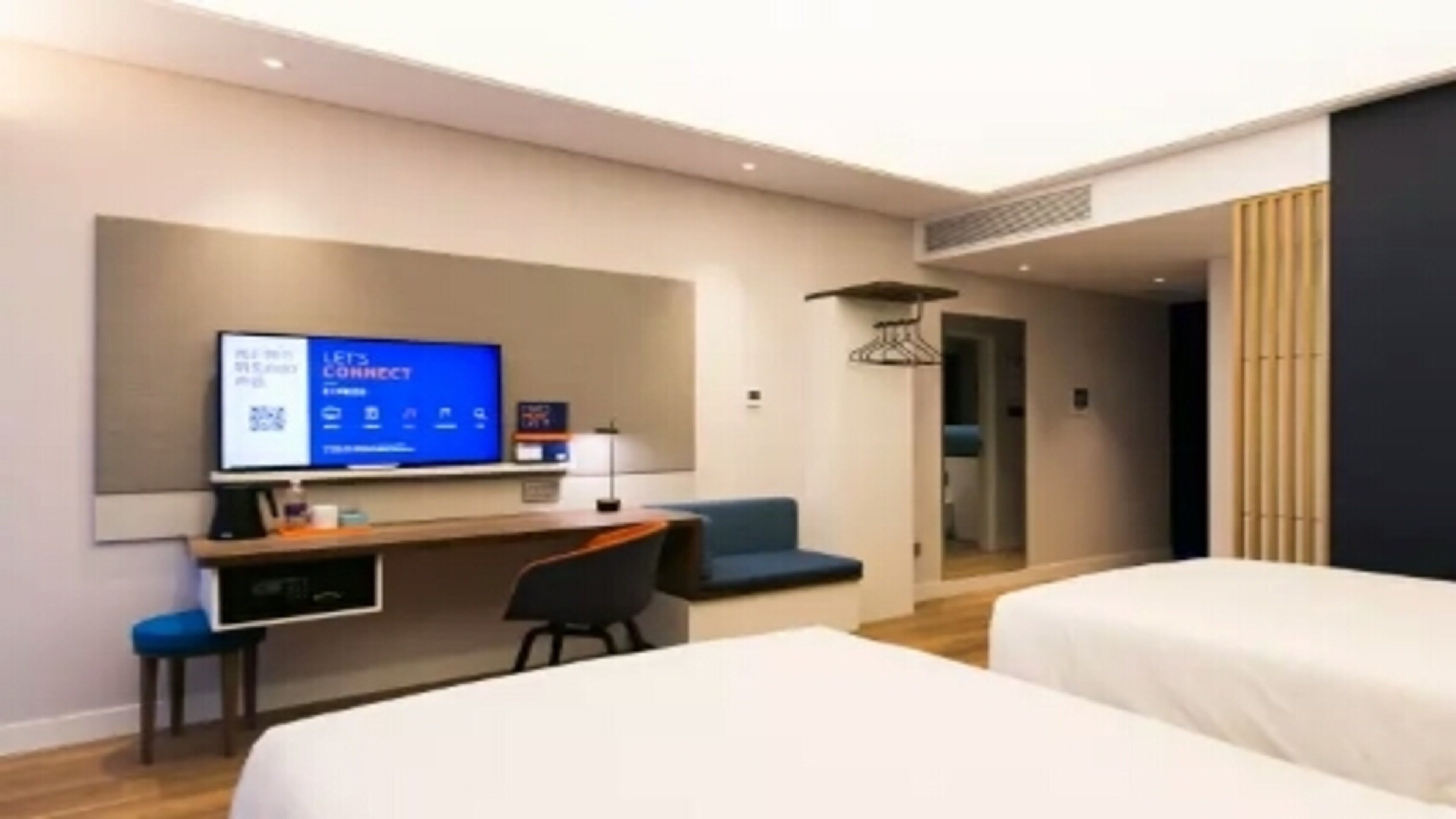 Una habitación de hotel moderna con una cama, un escritorio, una silla y un televisor mostrando un código QR.