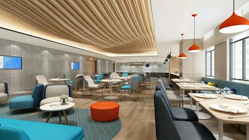 En moderne hotellobby med siddeområder, en receptionsdisk og udsigt til køkkenet.