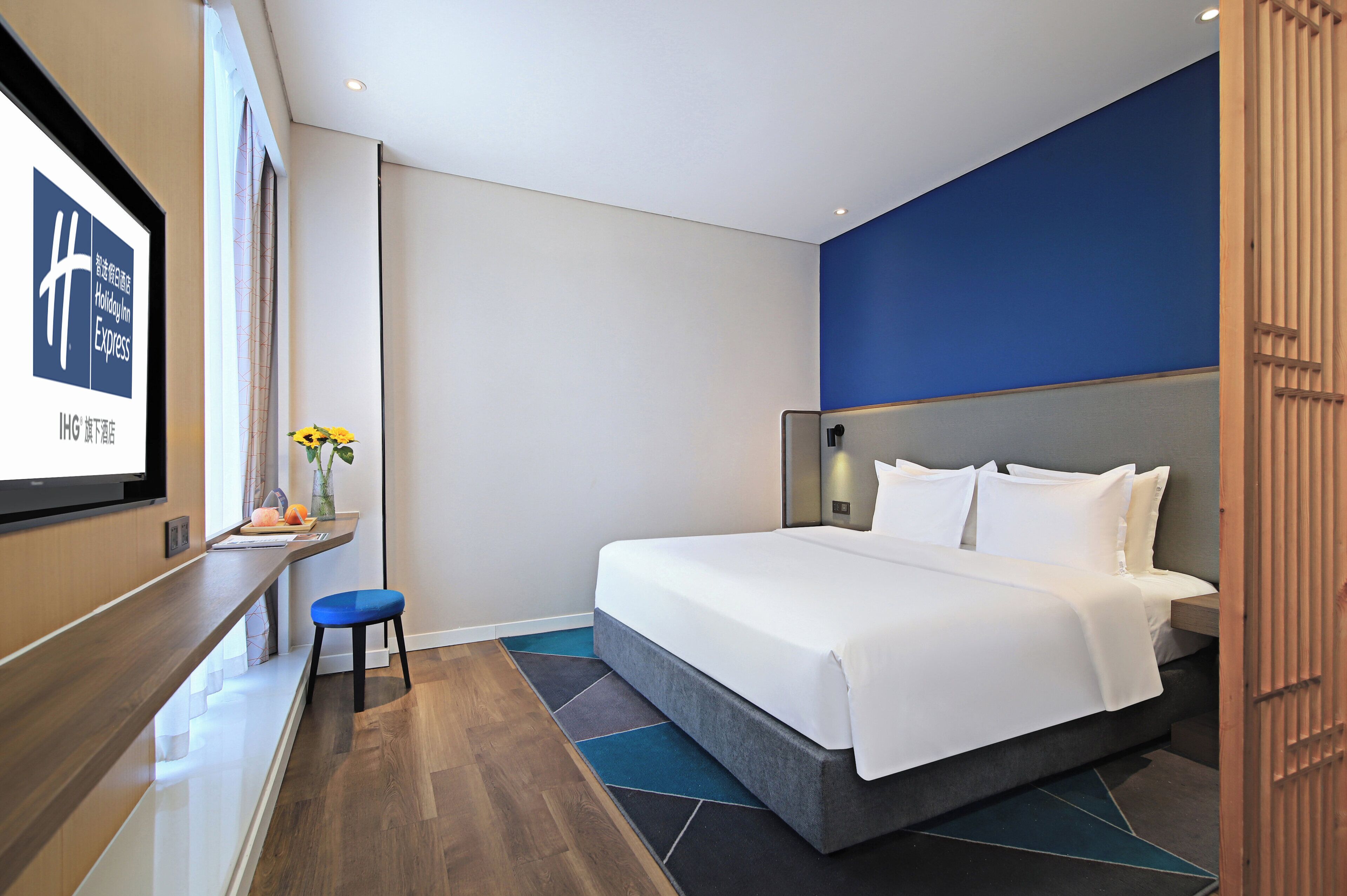A modern hotel room with a large bed, a small seating area, and a flat-screen TV on a wooden console.