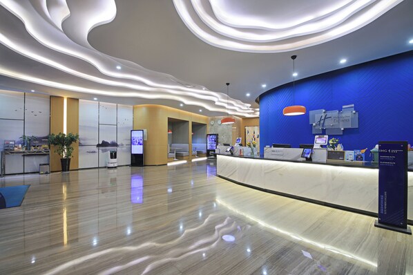 A modern hotel lobby with a curved reception desk, a blue accent wall, and a polished floor. - Holiday Inn Express Linyi West by IHG (Linyi)