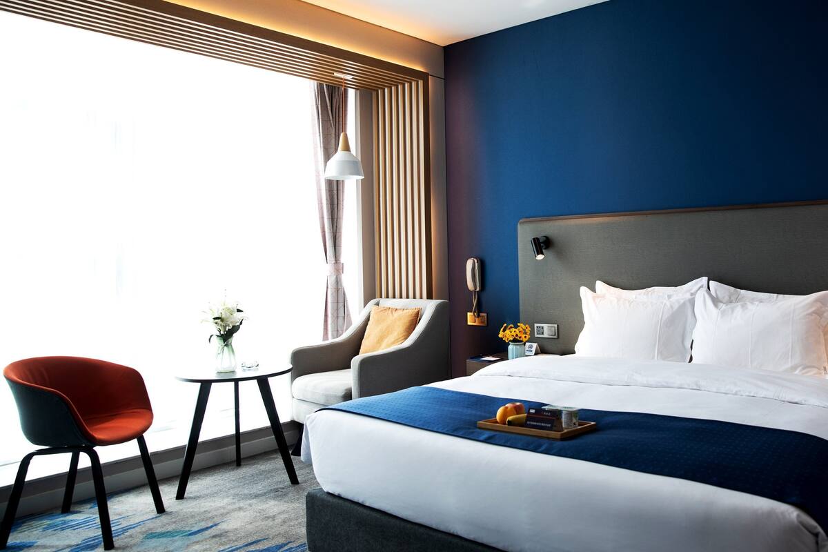 A hotel room with a large bed, a desk, a chair, and a window with curtains.