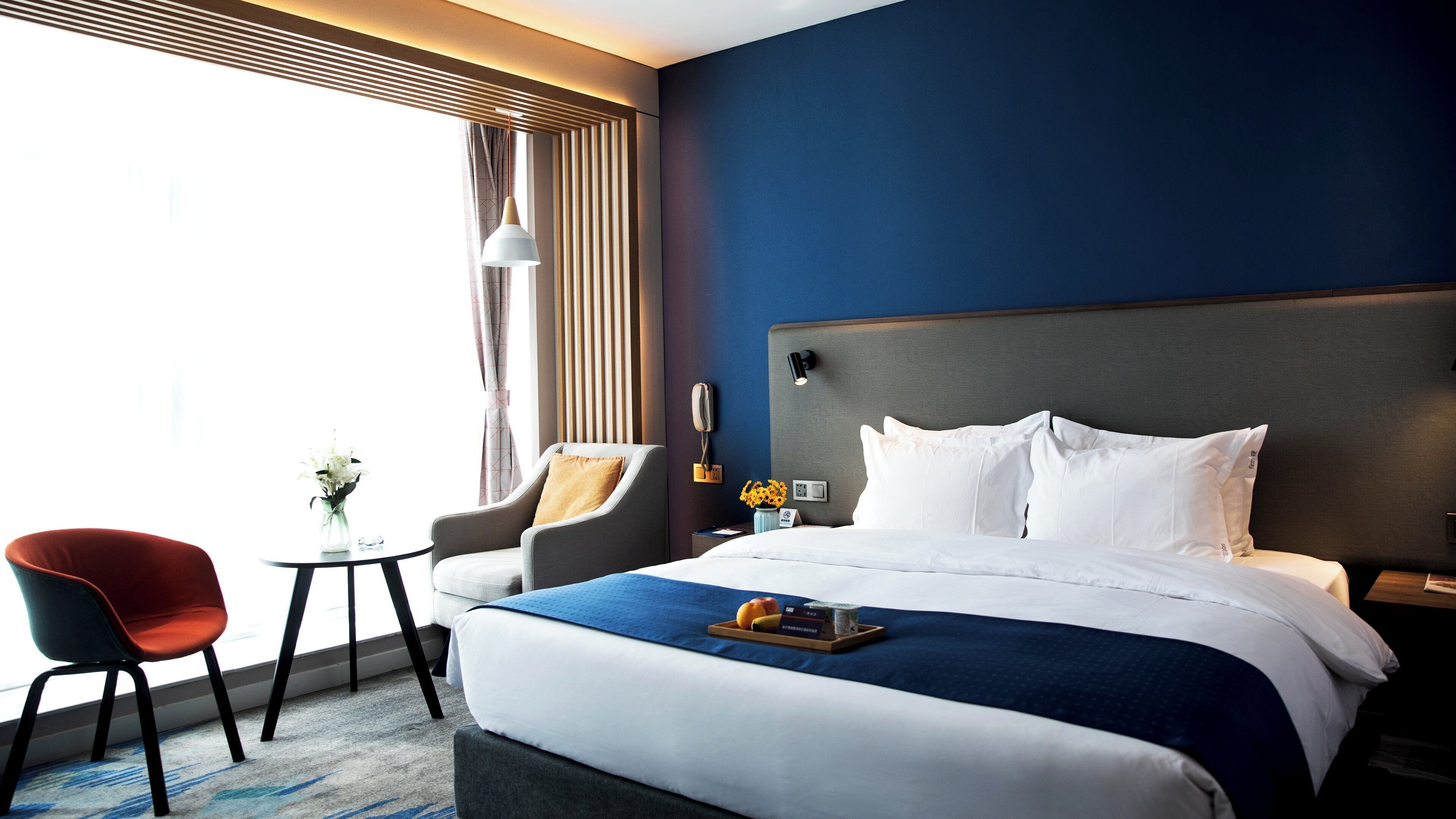 Una habitación de hotel con una cama grande, un escritorio, una silla y un ventanal con cortinas.