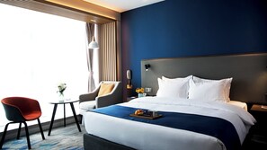 A hotel room with a large bed, a desk, a chair, and a window with curtains.