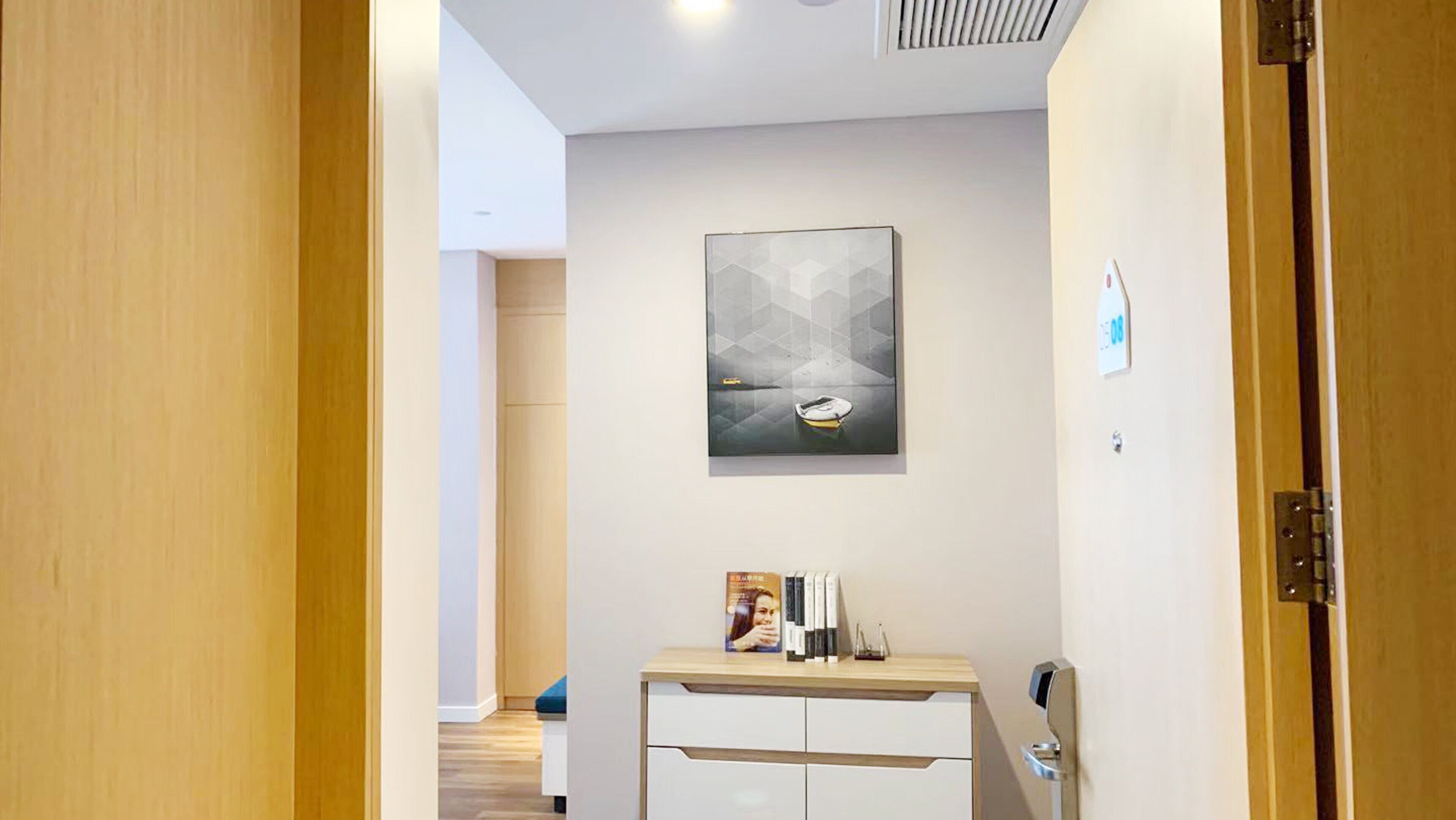Un couloir avec une porte en bois, un petit bureau avec des livres et une lampe, et un tableau représentant un bateau accroché au mur.
