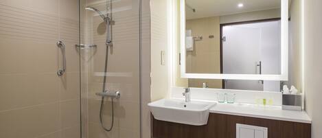 A modern bathroom with a glass-enclosed shower, a sink with a mirror above it, and neatly folded towels on a shelf.