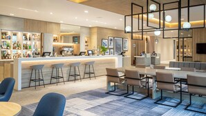 A modern bar area with a counter, stools, and a seating area with tables and chairs. - Courtyard by Marriott Inverness Airport (Inverness)