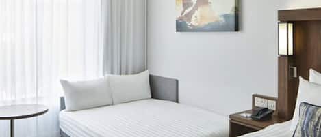 Habitación de hotel con dos camas, una mesita, una mesita de noche con un teléfono y un cuadro en la pared.