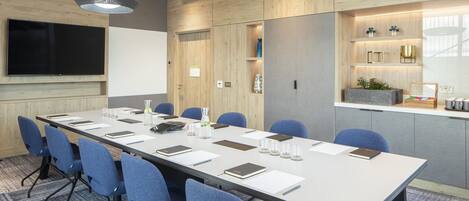 A conference room with a long table, blue chairs, a flat-screen TV, and pendant lights.
