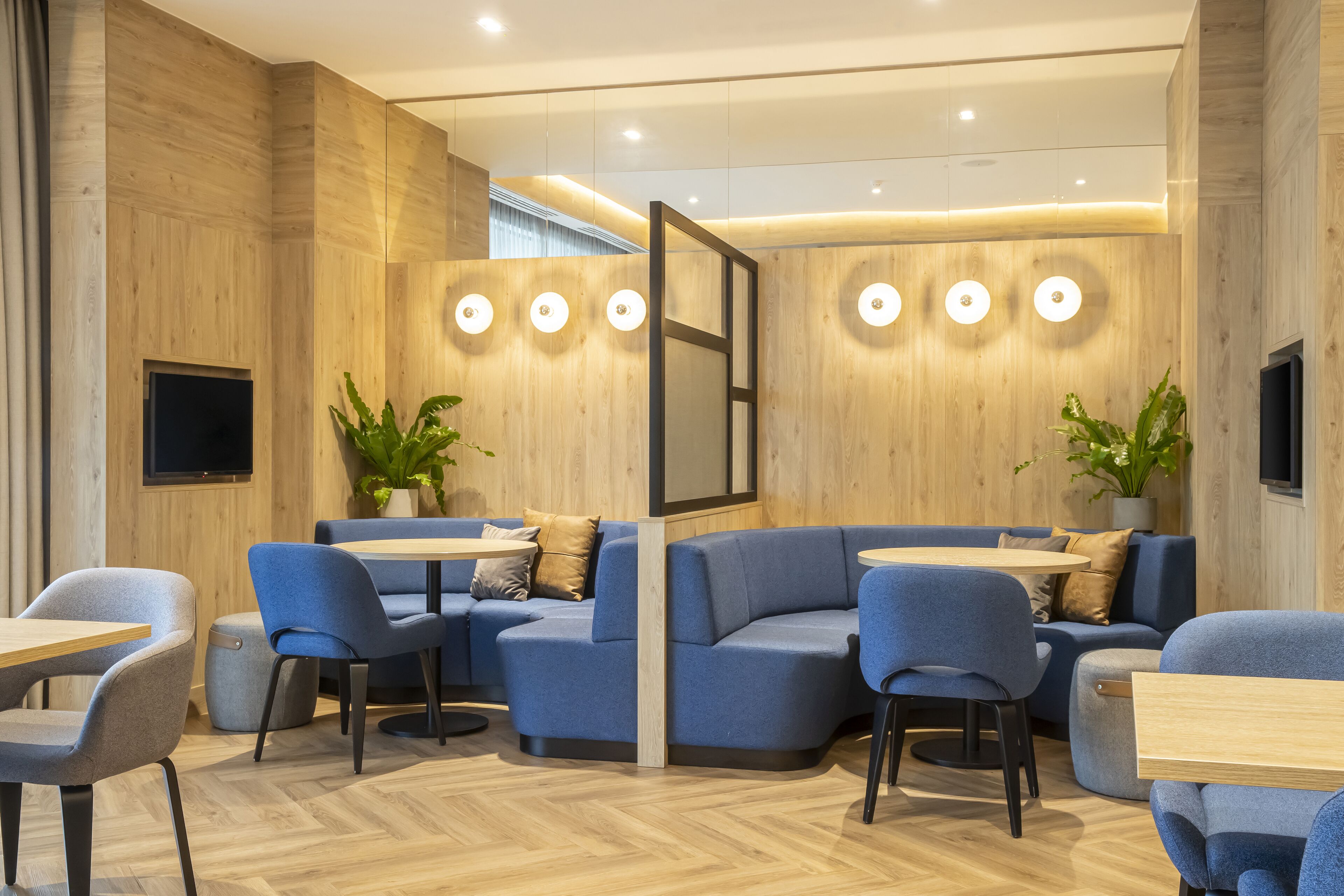 Decoração moderna com paredes de madeira, assentos azuis e mesas redondas.