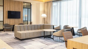 A modern hotel room with a sofa, chairs, a TV, and a lamp. - Courtyard by Marriott Inverness Airport (Inverness)