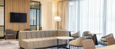 Quarto de hotel moderno com sofá, cadeiras, televisão e abajur.