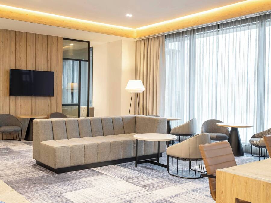 Una habitación de hotel moderna con sofá, sillas, televisor y lámpara.