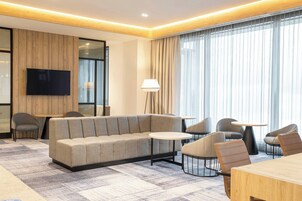 Una habitación de hotel moderna con sofá, sillas, televisor y lámpara.