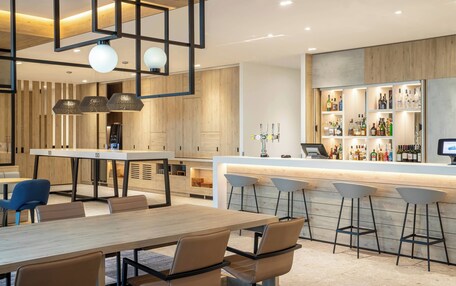 A modern bar area with a long counter, bar stools, and a variety of bottles.