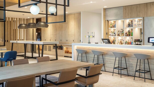 A modern bar area with a long counter, bar stools, and a variety of bottles. - Courtyard by Marriott Inverness Airport (Inverness)