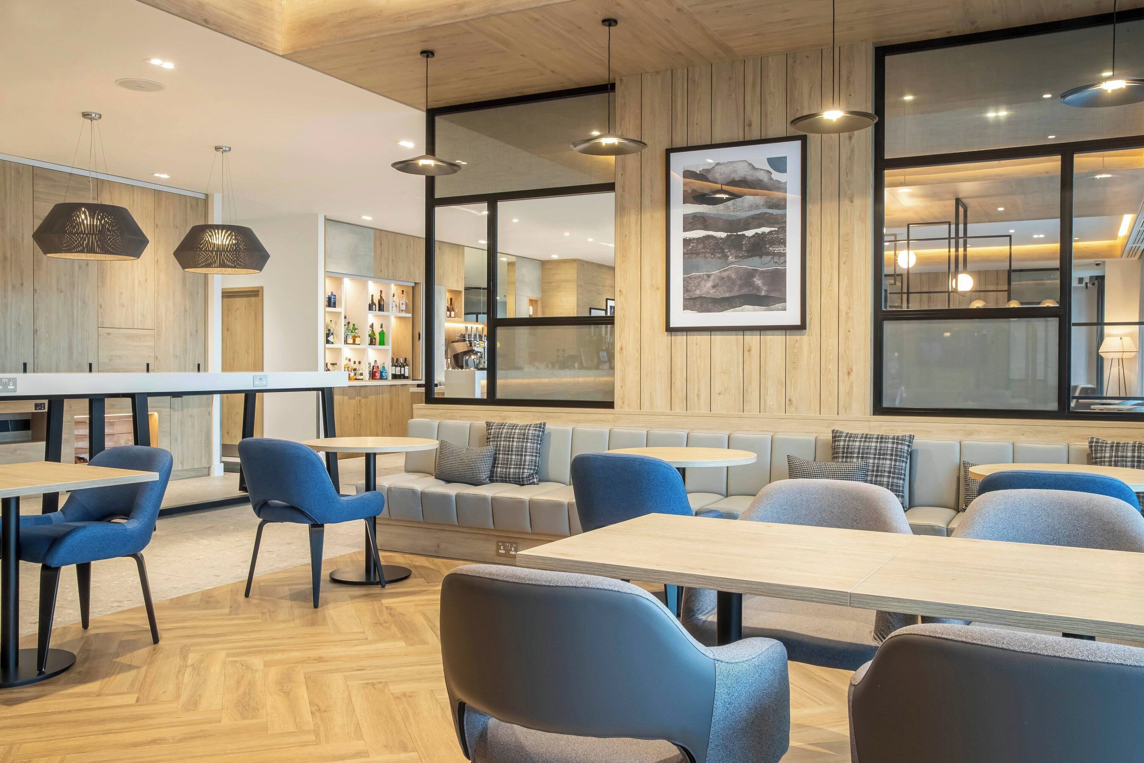 A modern restaurant with wooden walls, blue chairs, and a bar area.