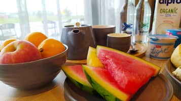 A breakfast table with a bowl of fruit, a teapot, a cup, and a carton of organic soya milk.
