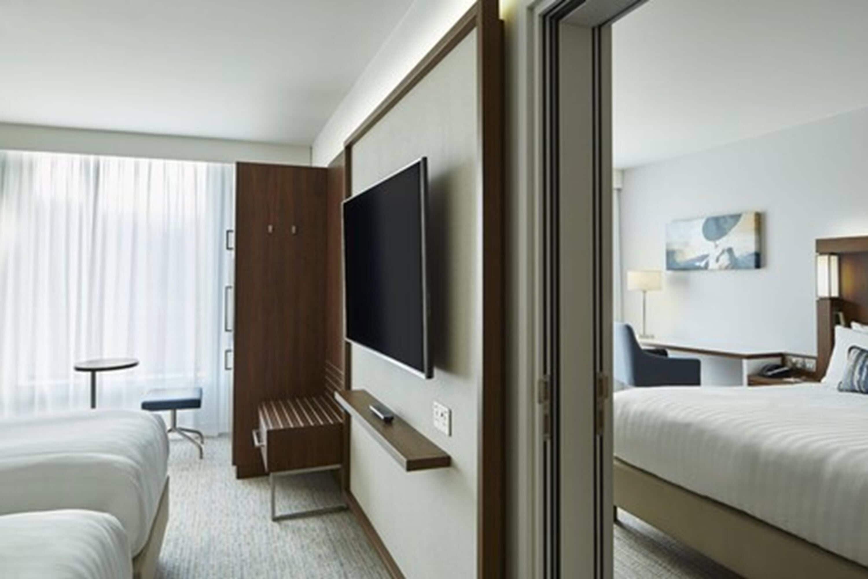 Habitación de hotel con cama, escritorio, televisión y ventana con cortinas.