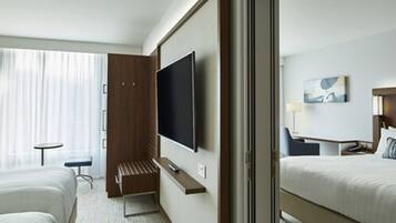 Habitación de hotel con cama, escritorio, televisión y ventana con cortinas.