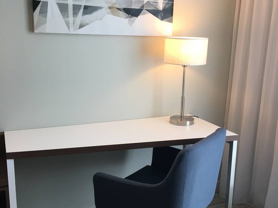 Una camera d'albergo con una scrivania, una sedia, una lampada e un quadro appeso al muro.