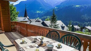 Eine Terrasse mit gedecktem Tisch für zwei Personen, mit Blick auf eine gebirgige Landschaft und einem Kirchturm.