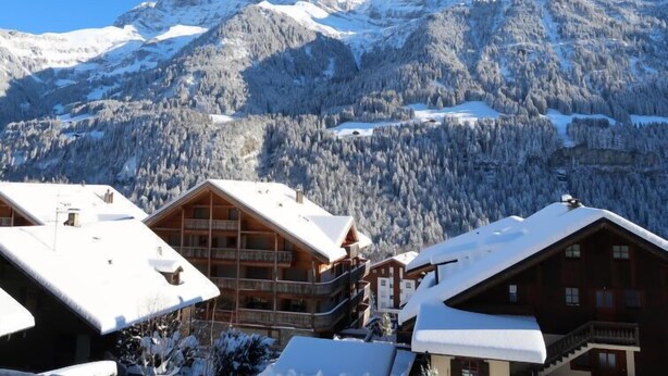 Eine Berglodge mit mehreren Balkonen und Blick auf schneebedeckte Gipfel.