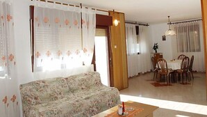 Un salon avec un canapé à motifs floraux, un coin repas avec une table et des chaises, et une cuisine équipée d’une cuisinière.