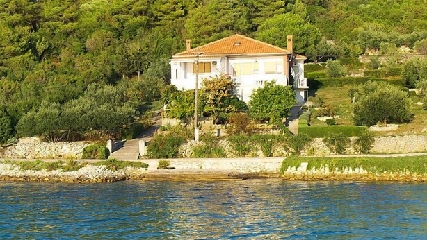 Une maison avec un toit en tuiles, entourée de verdure et bordée par un plan d’eau.