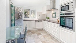 Une cuisine moderne avec des meubles blancs, un four à deux cavités et une table à manger en verre.