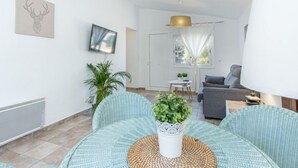 Un salon moderne avec un canapé, une table à manger et des chaises, un téléviseur fixé au mur et une plante sur la table.
