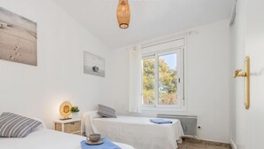 Une chambre avec deux lits, une fenêtre donnant sur des arbres, une table de chevet avec une lampe et un radiateur fixé au mur.