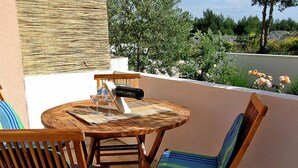 Un tavolo rotondo in legno con due sedie, una bottiglia e dei bicchieri su un balcone affacciato sul verde.