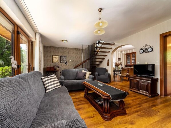 A spacious living room with a grey sofa, a wooden coffee table, and a TV stand.