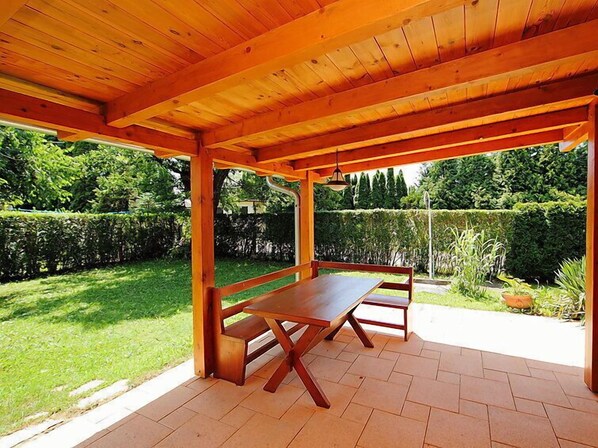 An outdoor wooden pergola with a table and benches, surrounded by a well-maintained garden and hedges.