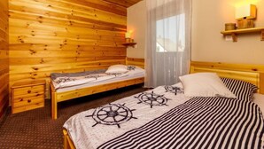 Une chambre de style cabane en bois, avec deux lits, une table de chevet, une fenêtre avec des rideaux et une étagère fixée au mur.