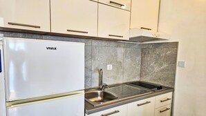 Una cocina compacta con un refrigerador VIVAX blanco, un lavamanos de acero inoxidable y un protector contra salpicaduras de mármol.