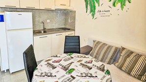 Una cocina compacta con armarios blancos, un refrigerador integrado y un lavamanos. Hay una mesa de comedor con mantel que muestra monumentos de la ciudad.