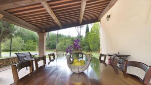 Eine überdachte Terrasse mit einem Holztisch, Stühlen und einer Obstschale.